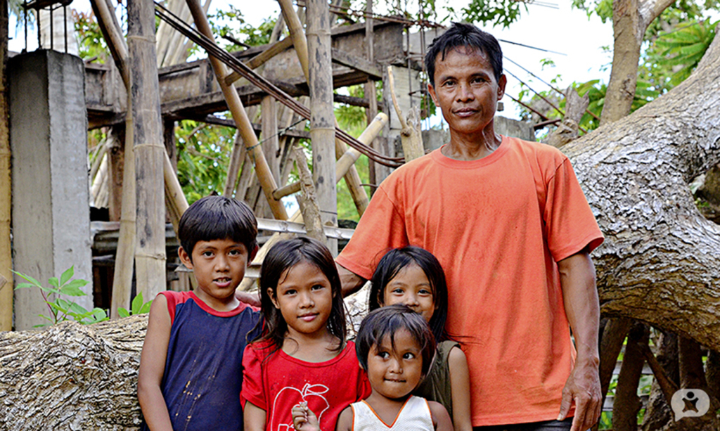 A fisherman in Bato, Camarines Sur with his children in front of his house and a fallen tree damaged by typhoon Nina.